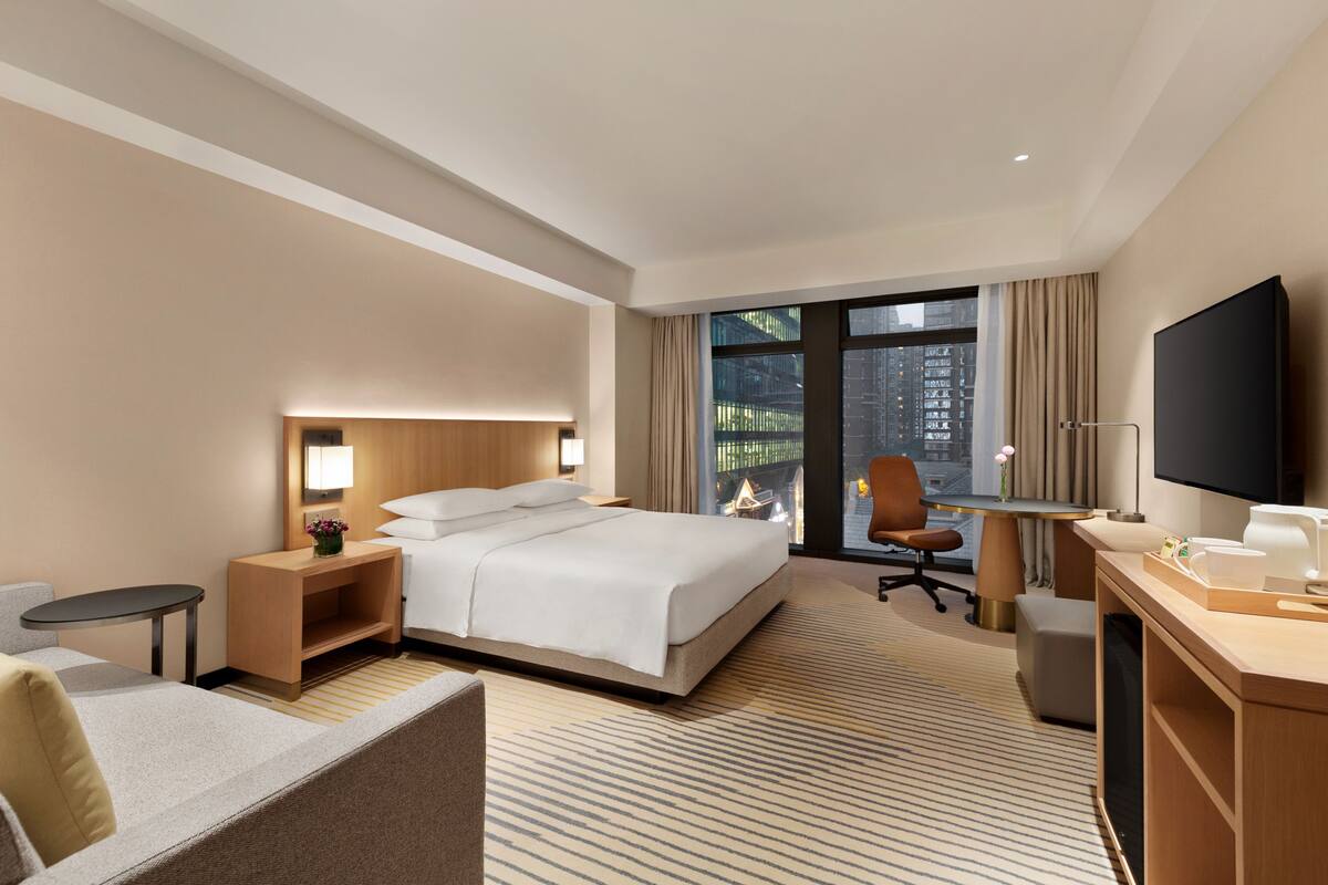 Quarto de hotel com cama, escrivaninha, cadeira, televisão e vista para a cidade.