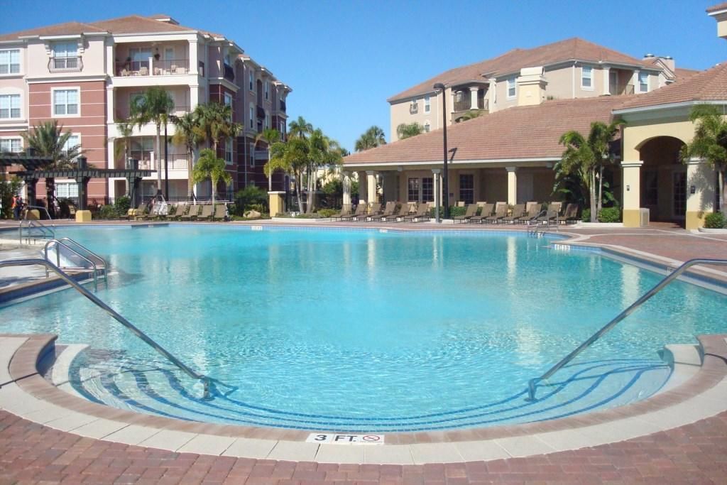 A swimming pool with a 3 FT depth marker, surrounded by lounge chairs and palm trees, with multi-story buildings in the background.