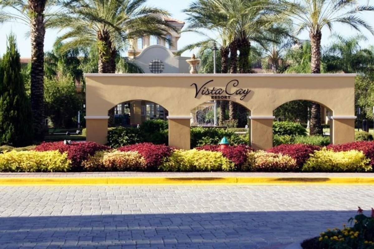 A Vista Cay Resort entrance with a beige archway, surrounded by well-maintained landscaping and palm trees.