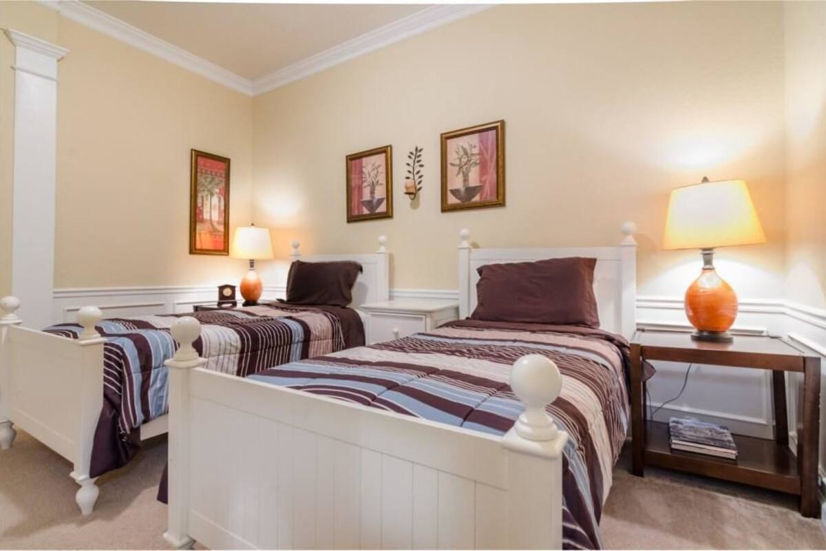 A hotel room with two single beds, a nightstand with a lamp, and wall-mounted artwork.