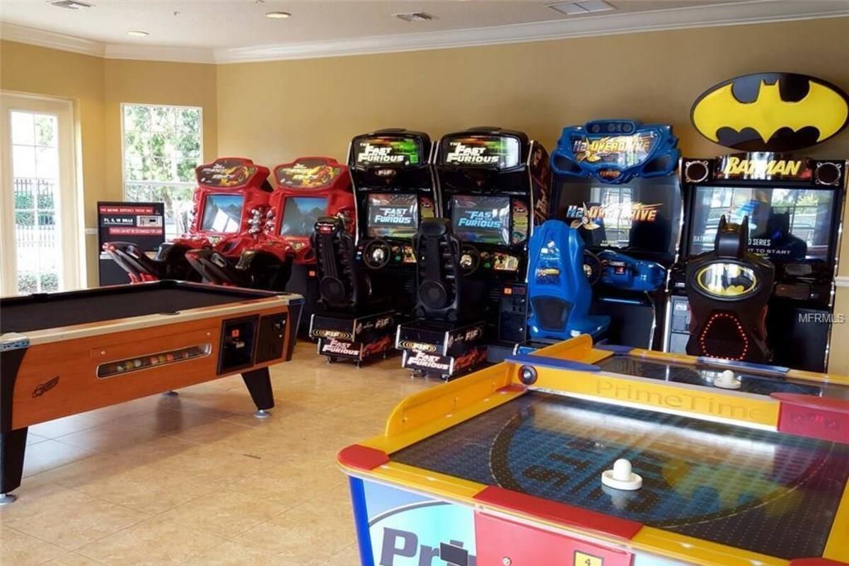 A pool table, arcade games including 'Fast Furious' and 'Batman', and a 'PrimeTime' game table in a room with beige walls and a tiled floor.