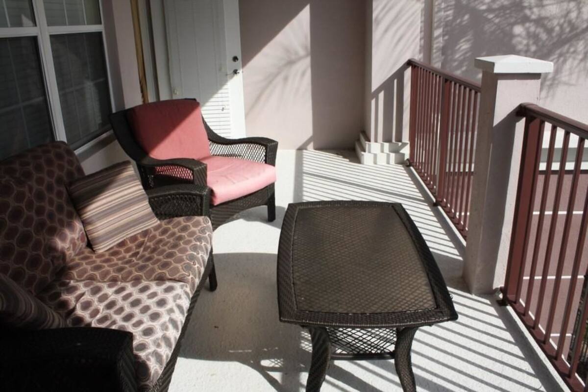 A balcony with a wicker sofa, a small table, and a red chair.