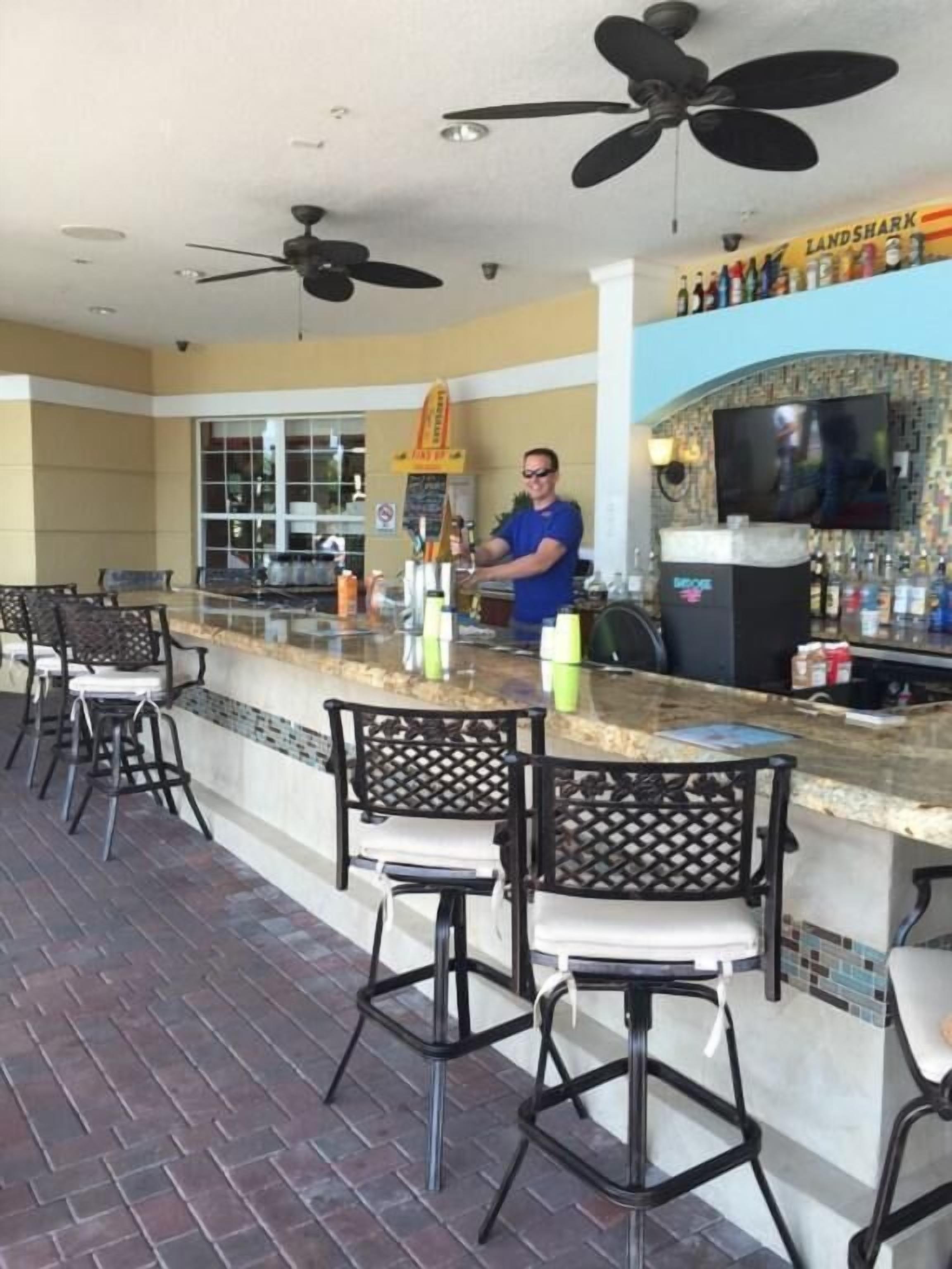 A bar area with a counter, bar stools, ceiling fans, and a television screen.