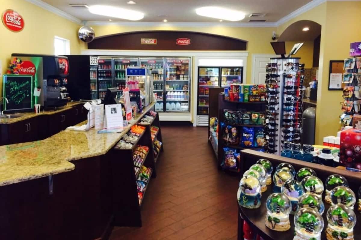 L’intérieur d’un magasin, avec un réfrigérateur Coca-Cola, des étagères remplies de snacks et un présentoir de verres originaux.