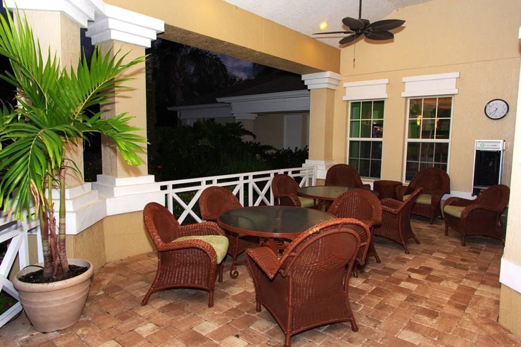 An outdoor patio with wicker furniture, a potted plant, and a clock on the wall.