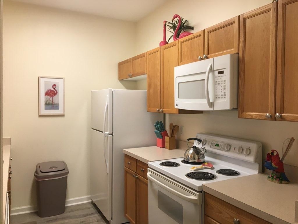 A compact kitchen with wooden cabinets, a white microwave, a stove, and a refrigerator.