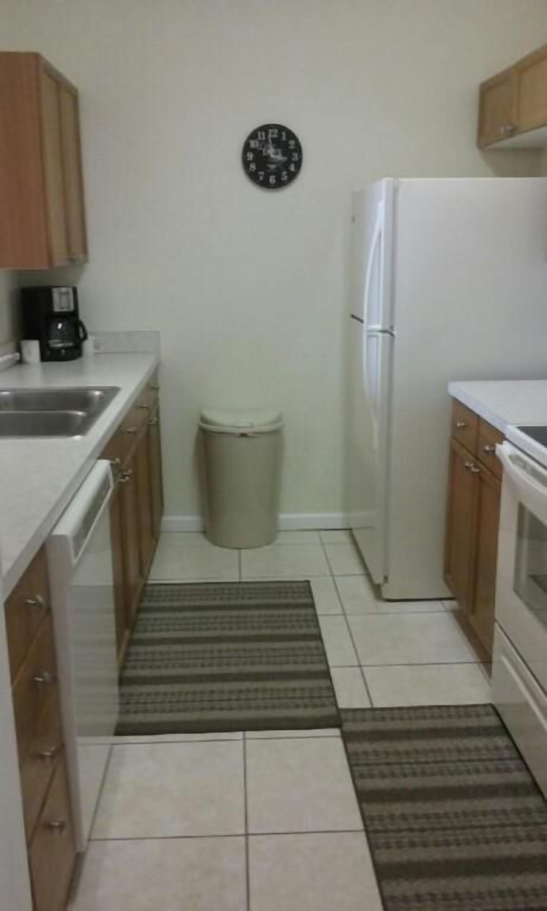 A small kitchen with wooden cabinets, a white refrigerator, a coffee maker, and a trash can.