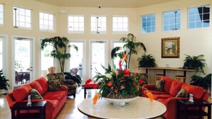 A spacious living room with a round coffee table, red sofas, and large windows allowing natural light. - Windsor Palms Resort (Kissimmee)