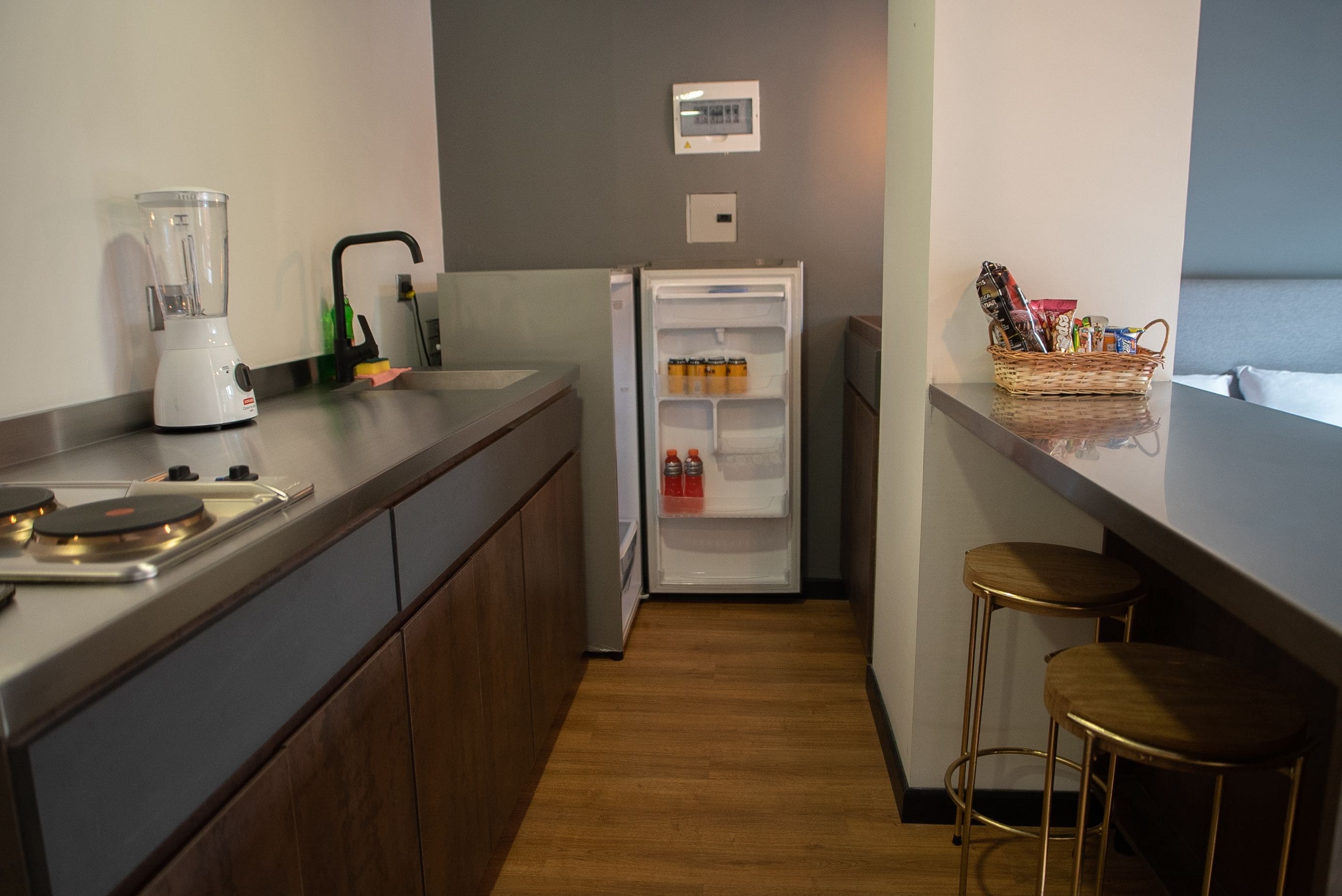 Eine kleine Küche mit Mixer, Kühlschrank, Spüle und einem Barhocker.