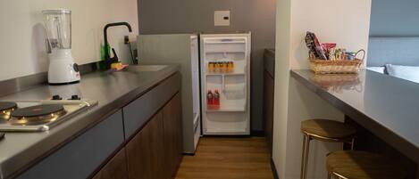 Eine kleine Küche mit Mixer, Kühlschrank, Spüle und einem Barhocker.