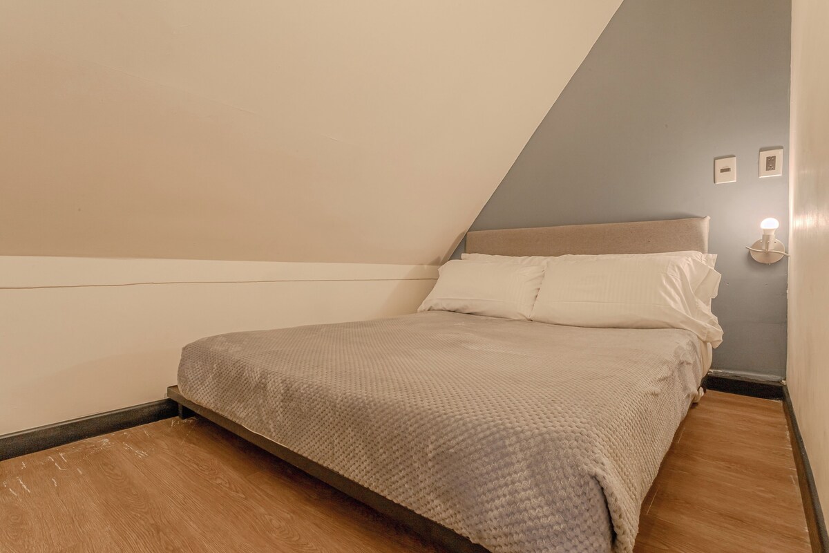 A bedroom with a bed, a nightstand, and a wall-mounted light.
