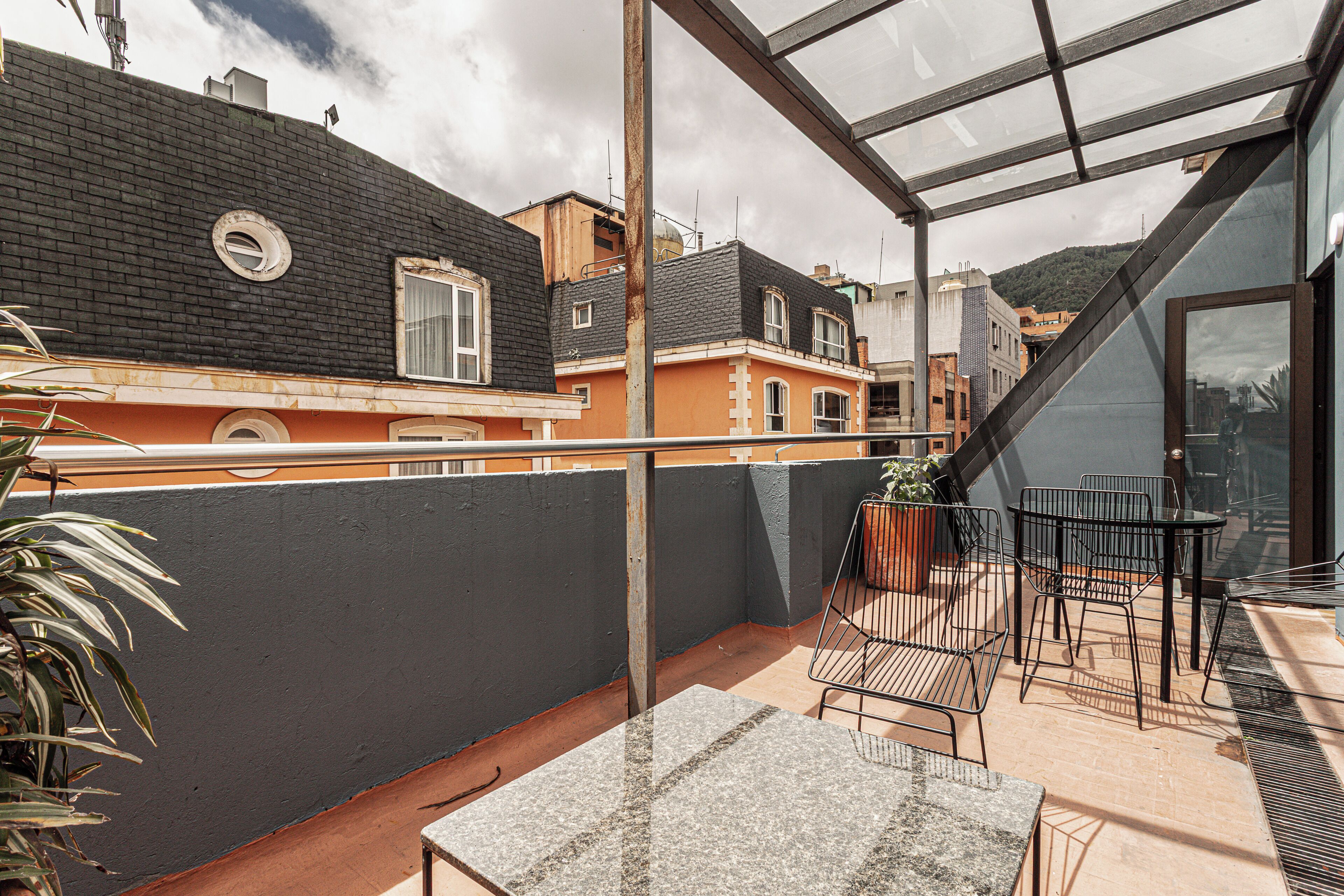 A rooftop terrace with a glass enclosure, outdoor seating, and a view of neighboring buildings.