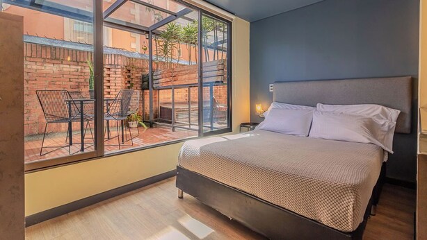 A bedroom with a large window, a bed, and a small table with chairs.