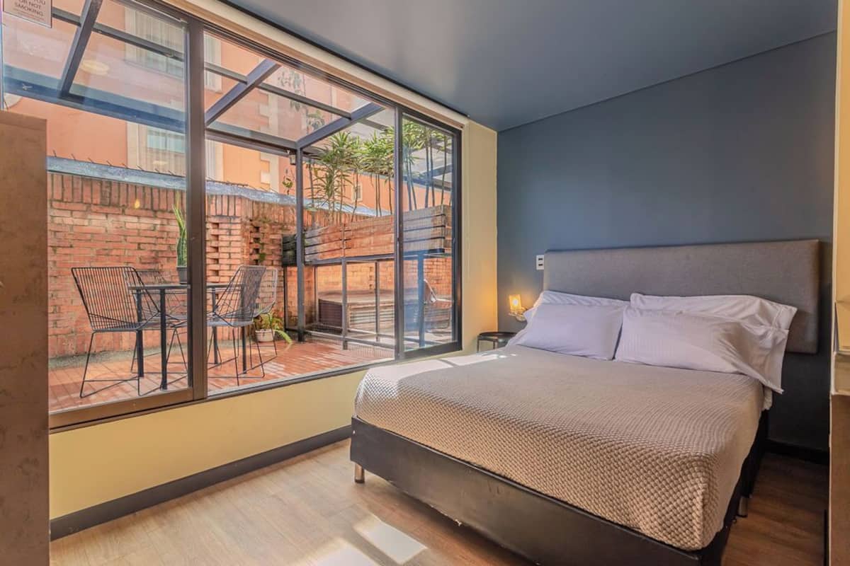 Un dormitorio con un ventanal grande, una cama y una pequeña mesa con sillas.