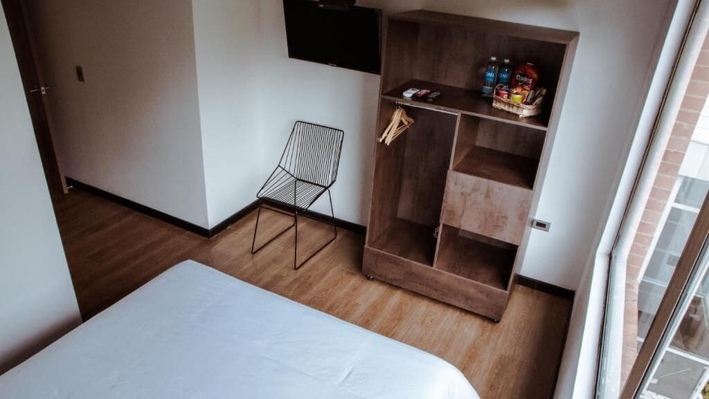 Ein Zimmer mit einem Bett, einem Sessel, einem Holzschrank und einem Fernseher an der Wand.