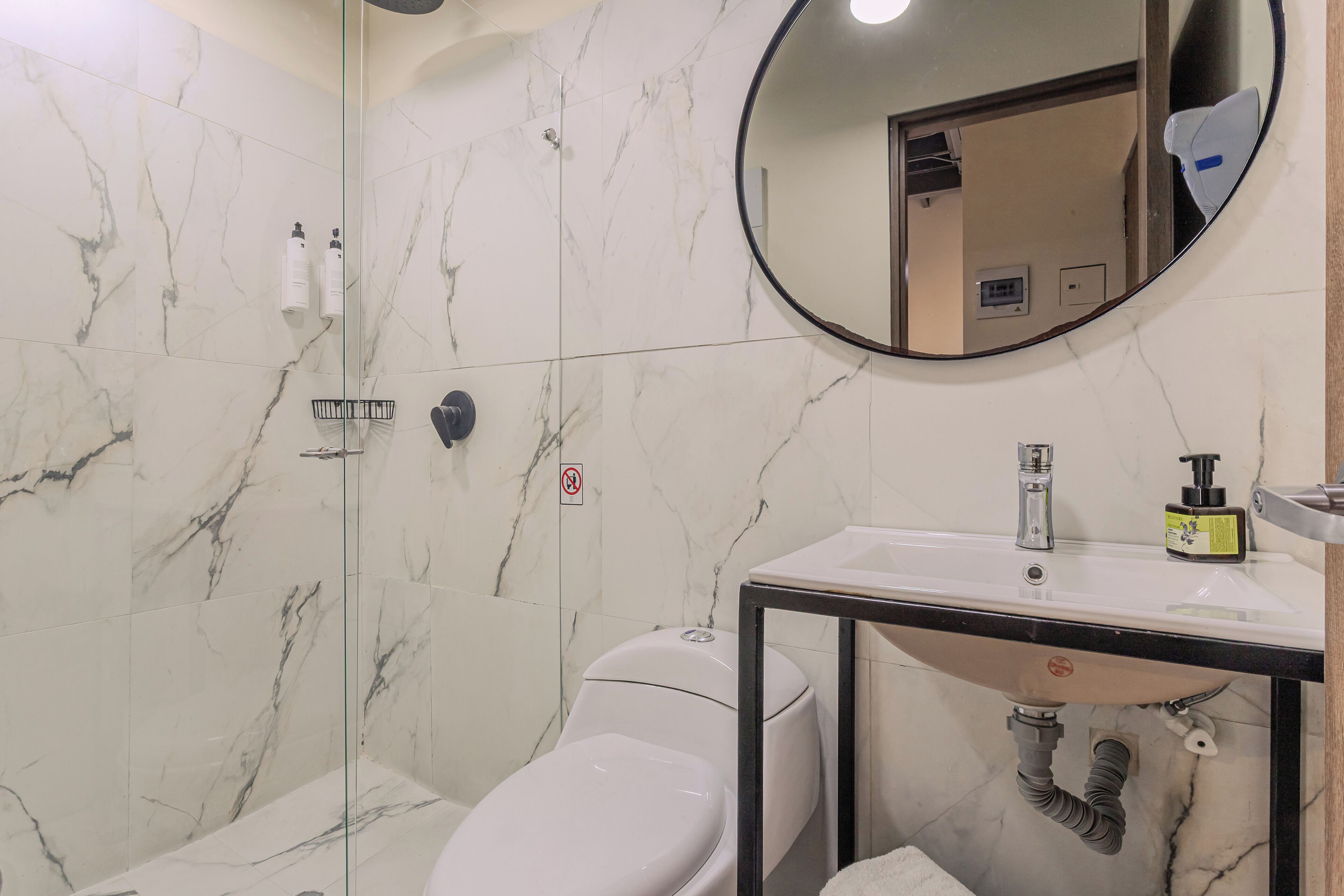 Een badkamer met een marmeren wand, toilet, wastafel en douche.