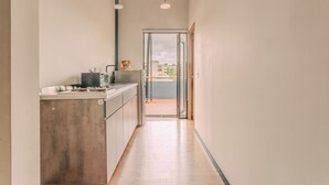 A narrow hallway with a kitchen area on the left, a door leading to an outdoor balcony, and a view of buildings outside.