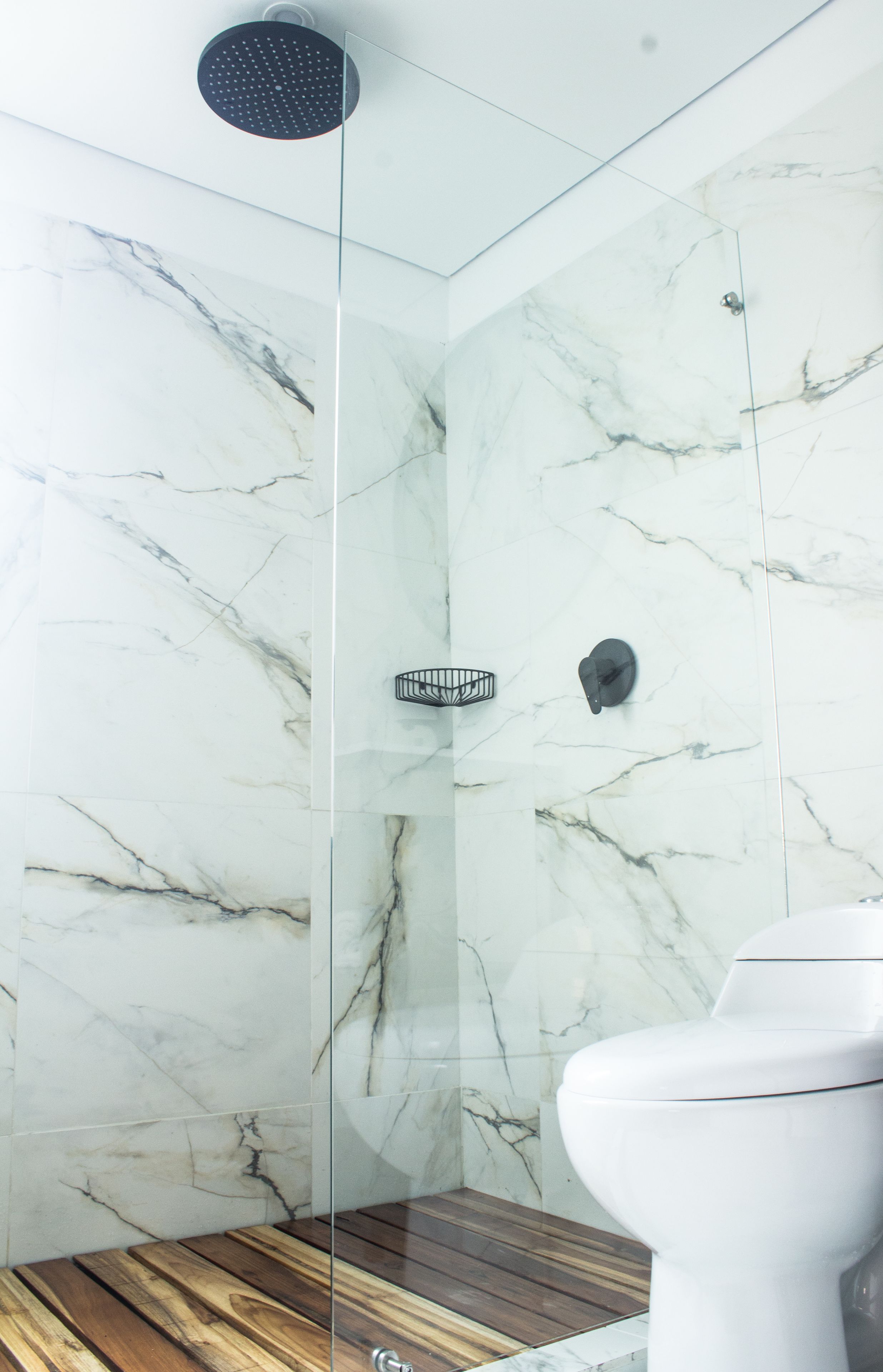 A modern bathroom with a glass-enclosed shower, marble walls, and a wooden floor.