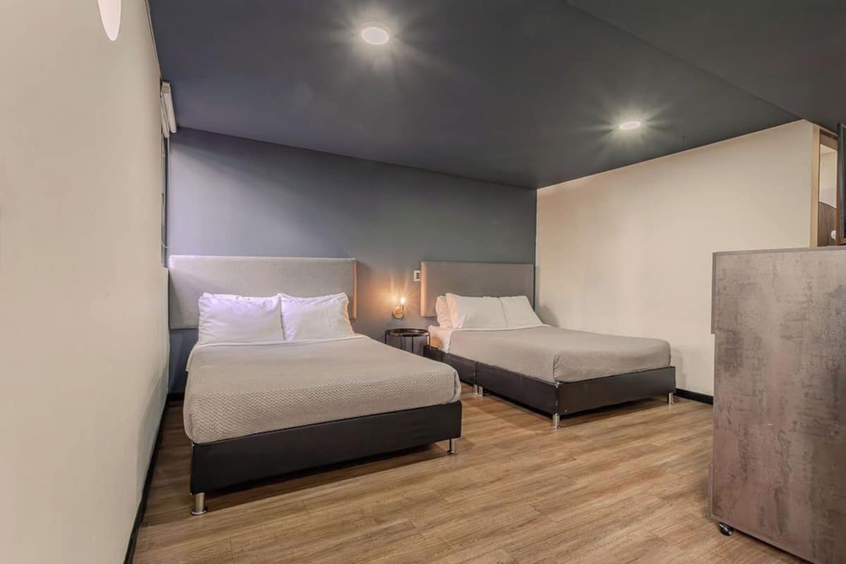 Habitación de hotel con dos camas, una mesita de noche pequeña, una lámpara de pared y un armario.