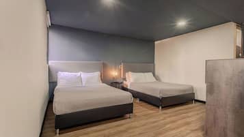 Habitación de hotel con dos camas, una mesita de noche pequeña, una lámpara de pared y un armario.