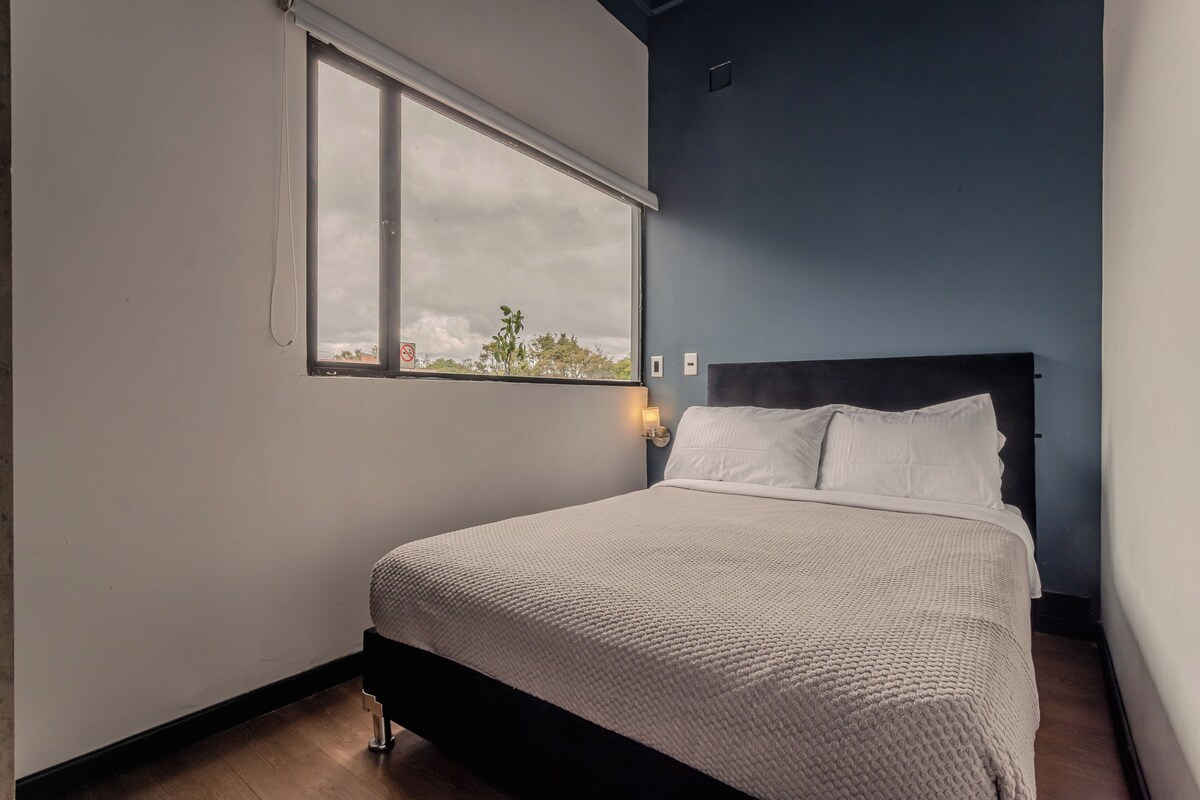 A bedroom with a bed, a window, and a wall-mounted light.