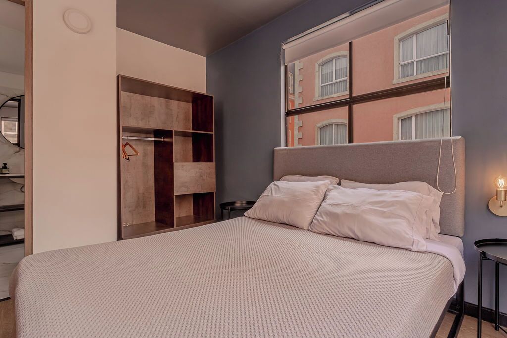 Een slaapkamer met een bed, een kledingkast en uitzicht op gebouwen door een raam.