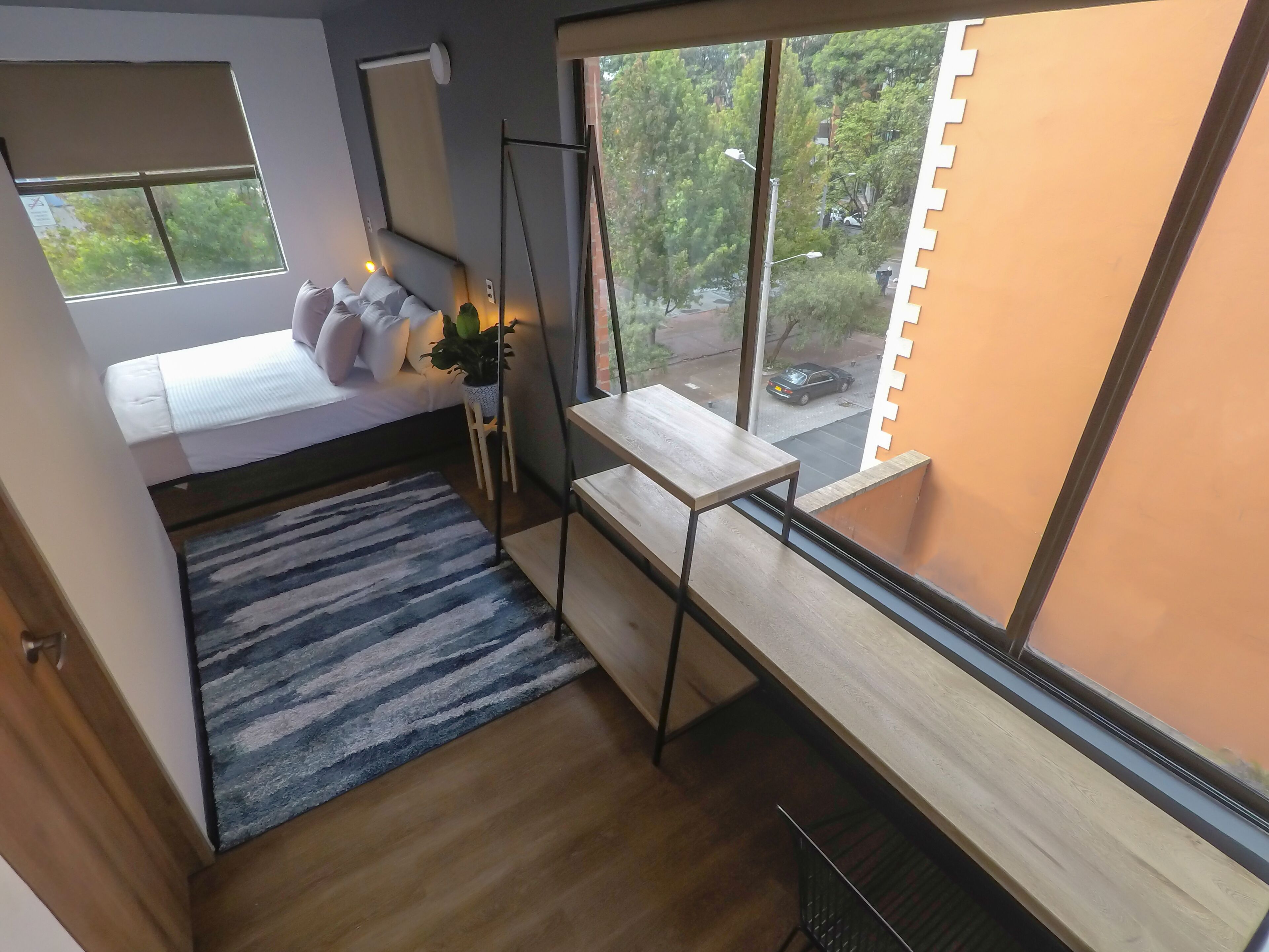 A compact bedroom with a bed, a small desk, a window, and a view of the outdoors.