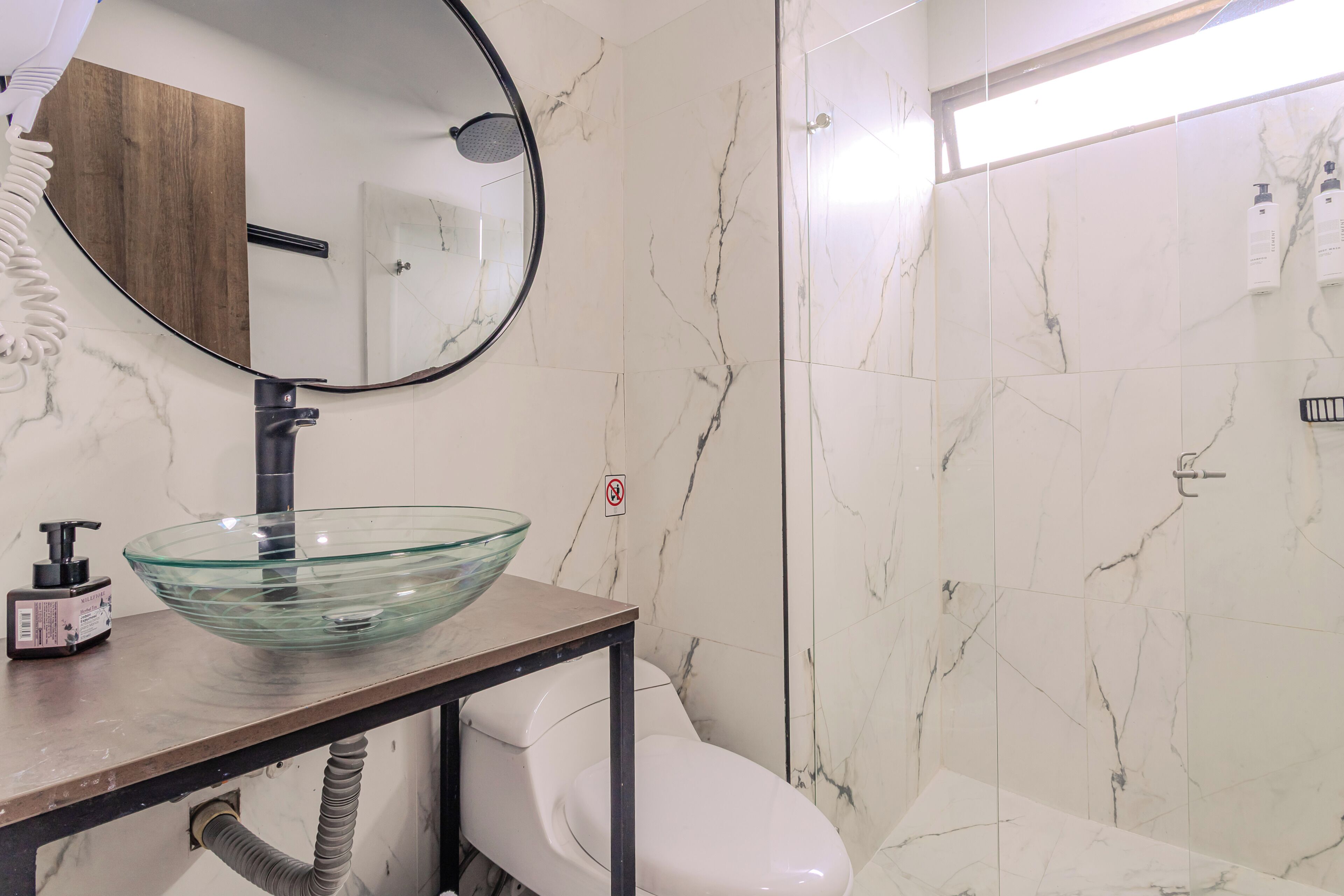 Un baño con lavamanos de vidrio, inodoro, espejo y zona de ducha.