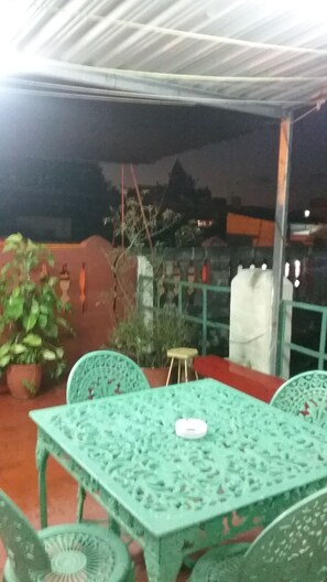 Ein Außenbereich mit einer Terrasse, einem Tisch, Stühlen, einem Blumentopf und einem kleinen Hocker.