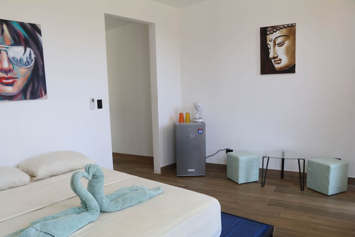 A hotel room with a bed, a refrigerator, a small table, and two ottomans.