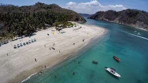 An aerial view of a beach with clear turquoise waters, a sandy shore, and a dense forested area. - La Jolla Hotel (Cóbano)