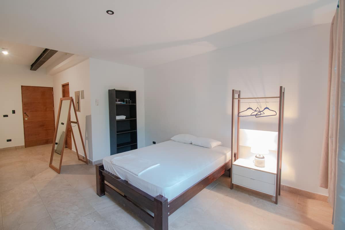 A bedroom with a wooden bed, a wardrobe, a mirror, and a clothing rack.