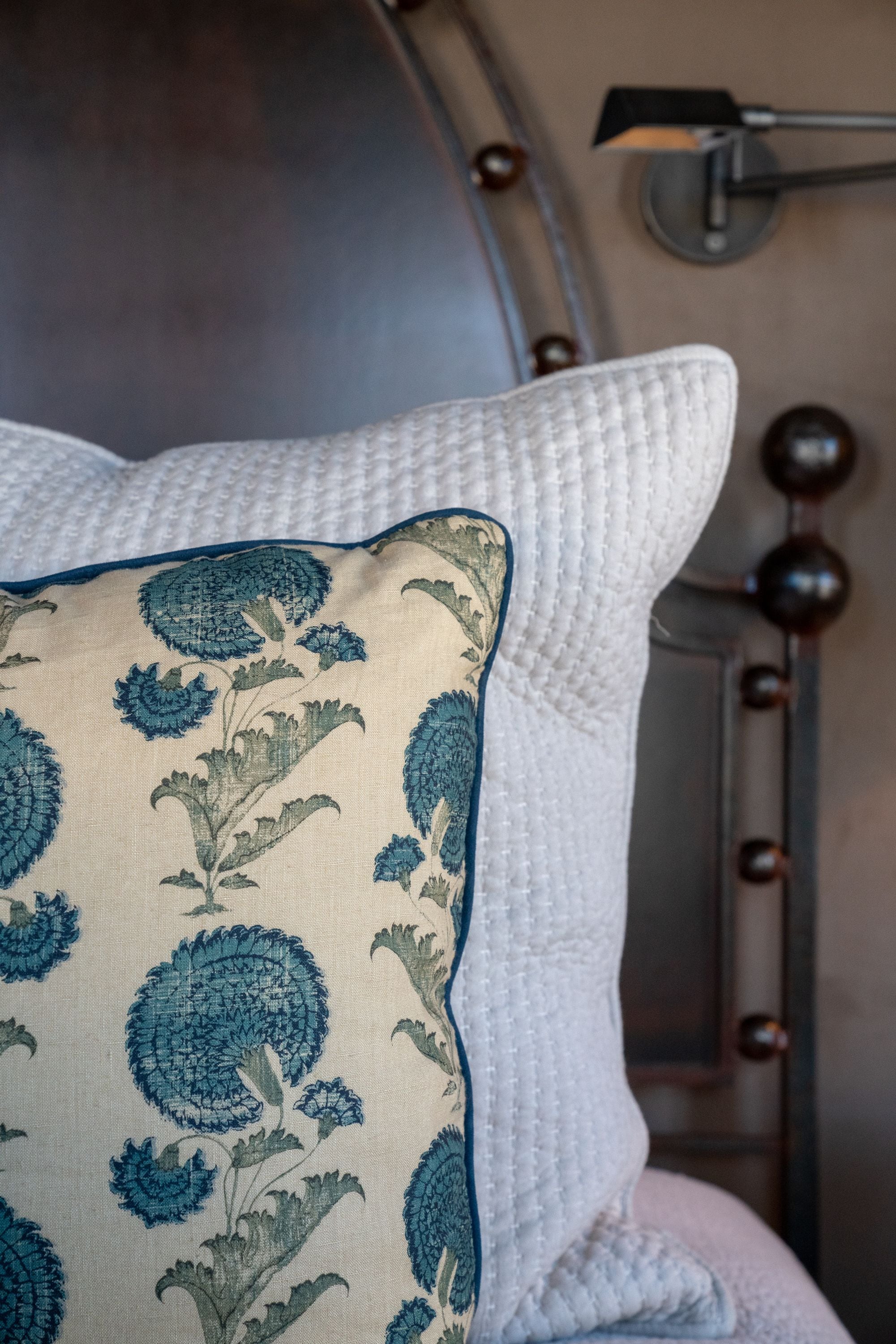 Una cama con un almohadón blanco y un cojín decorado con un estampado floral.