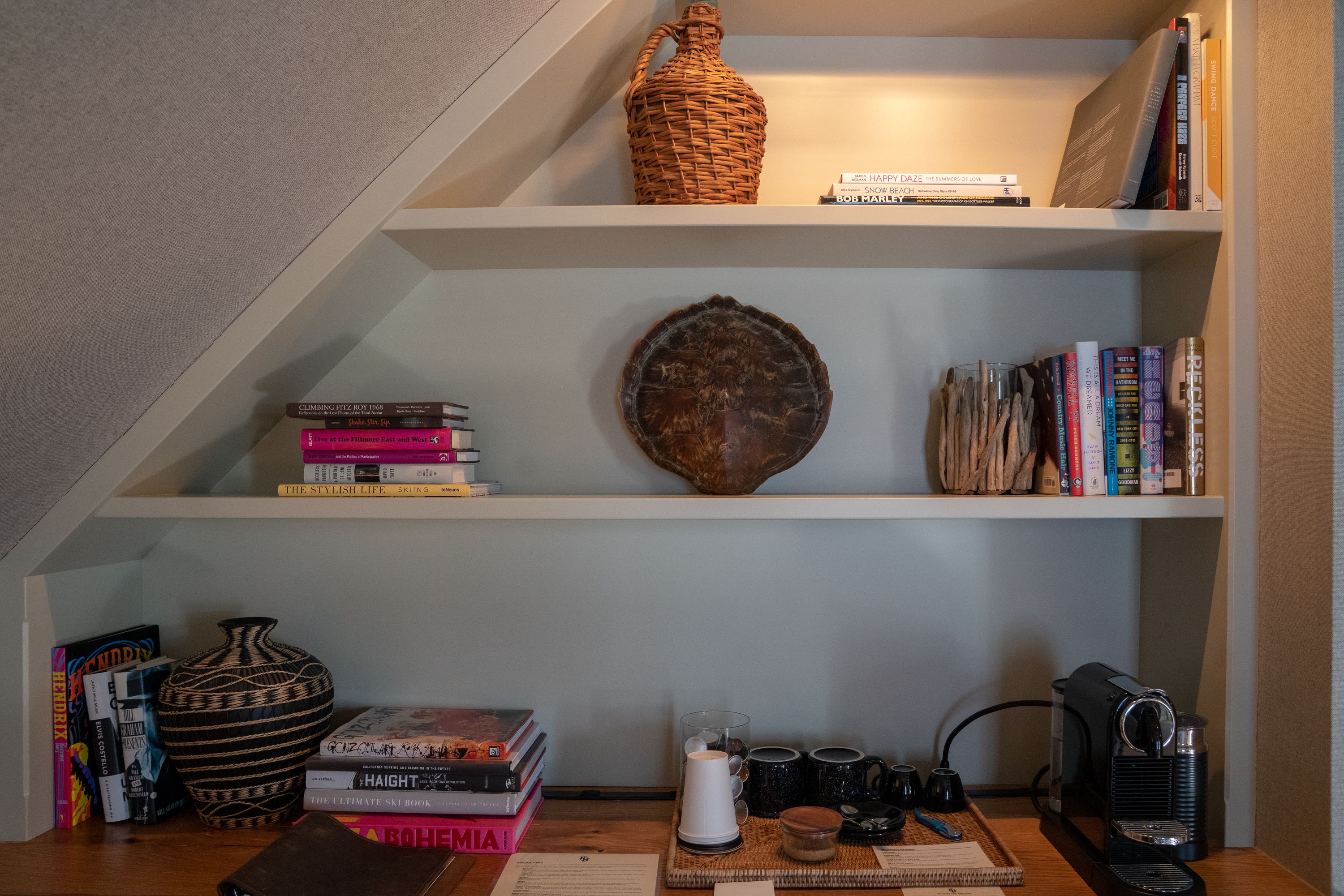 Una estantería con libros, un jarrón decorativo y una cafetera.