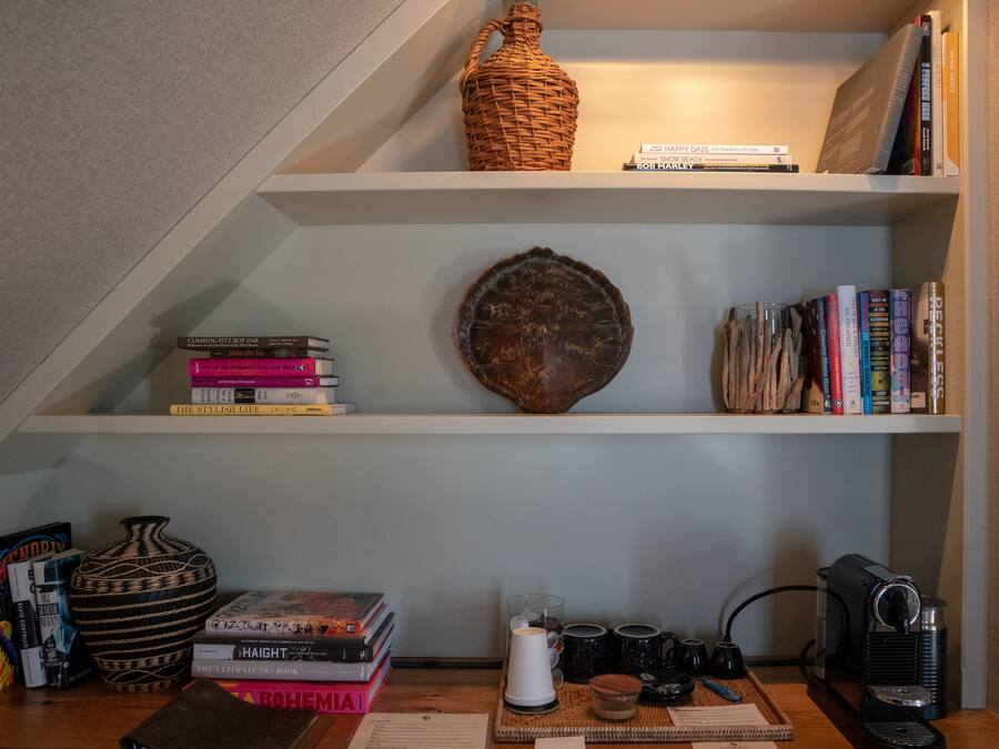Una estantería con libros, un jarrón decorativo y una cafetera.