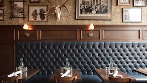 A restaurant interior with a tufted leather bench, wooden tables, and framed pictures on the wall. - Public House Lofts (Crested Butte)