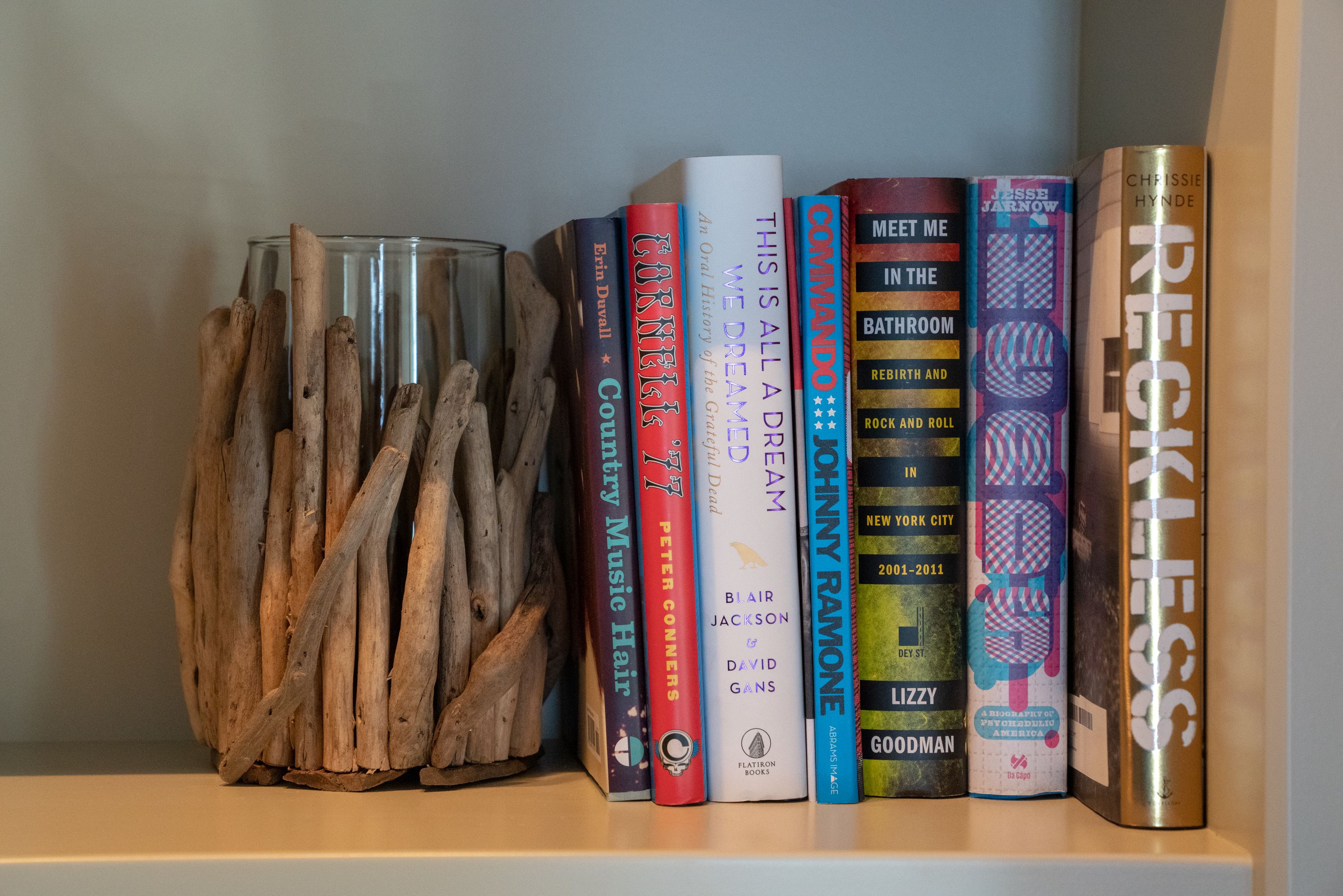 Una estanteria amb llibres i un vas de vidre amb branques.