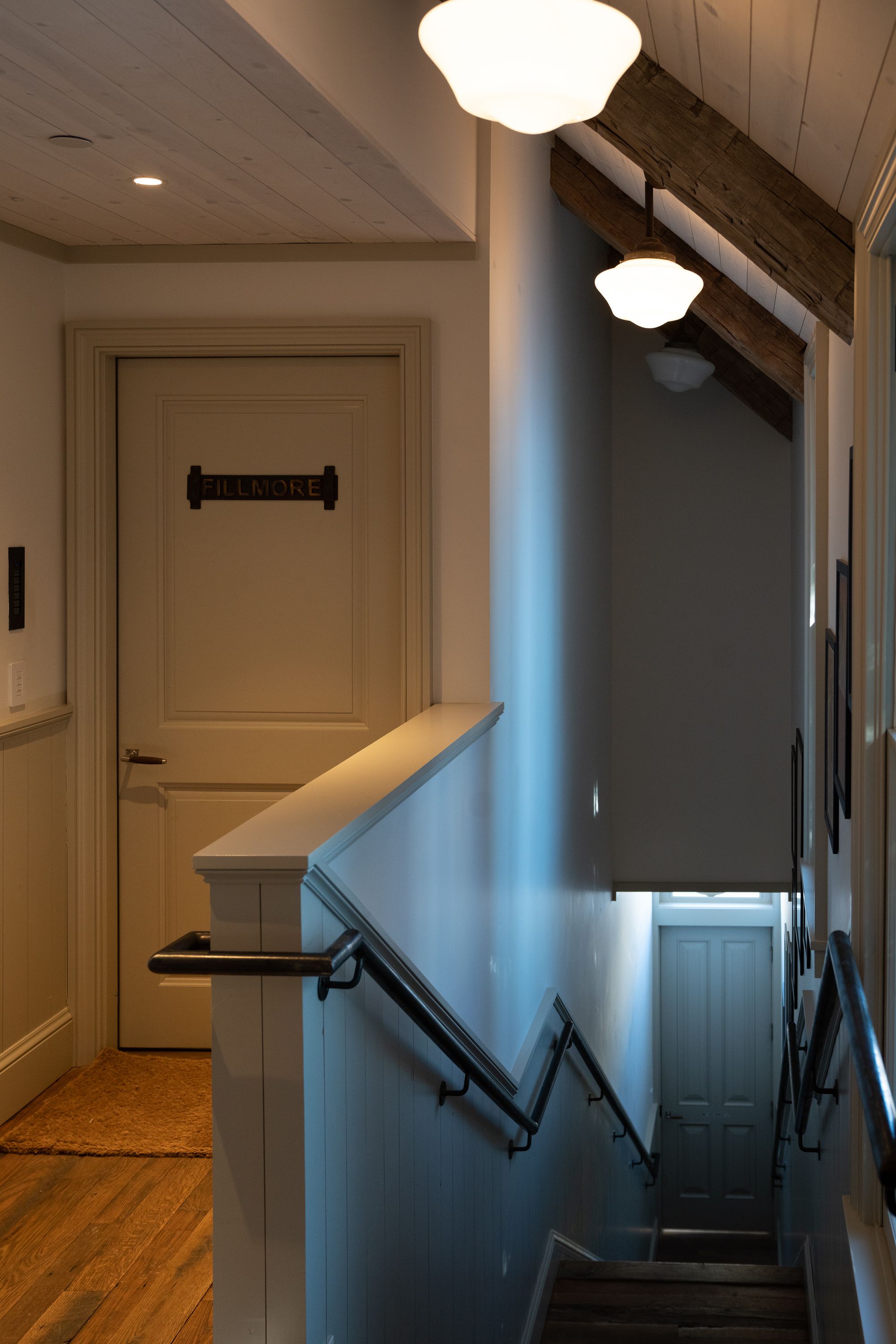 Una escalera de madera con barandillas negras que conduce a una puerta con un letrero encima.