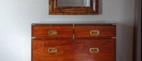 A wooden dresser with brass handles and a mirror above it, against a plain wall.