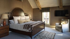 A bedroom with a large bed, wooden beams, a TV, and a window with a view. - Public House Lofts (Crested Butte)