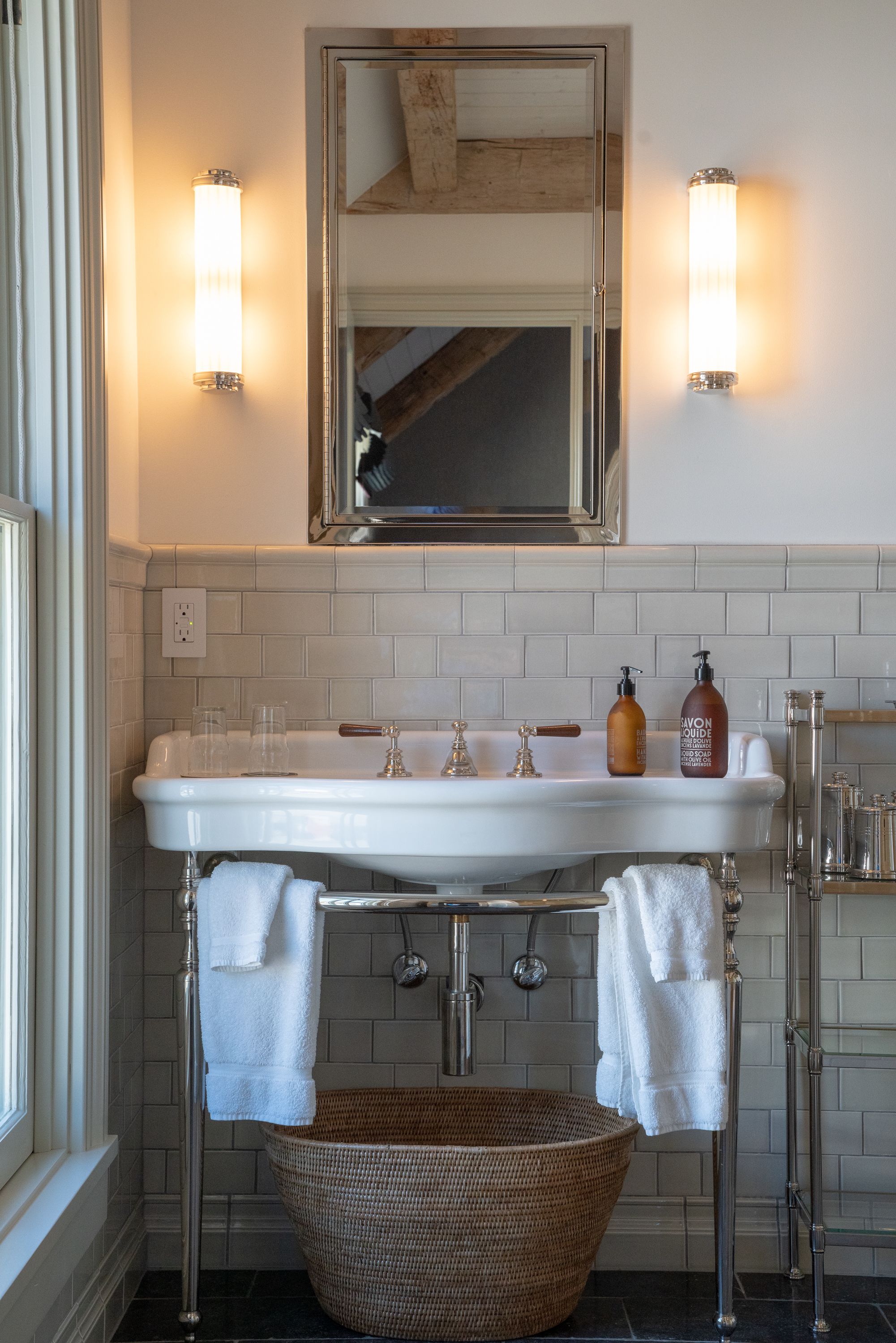 Un baño con lavamanos blanco, dos luces empotradas, un espejo y una cesta de mimbre.