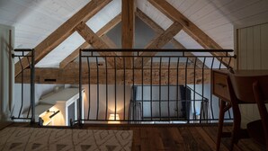 A loft bedroom with exposed wooden beams, a metal railing, and a small window. - Public House Lofts (Crested Butte)