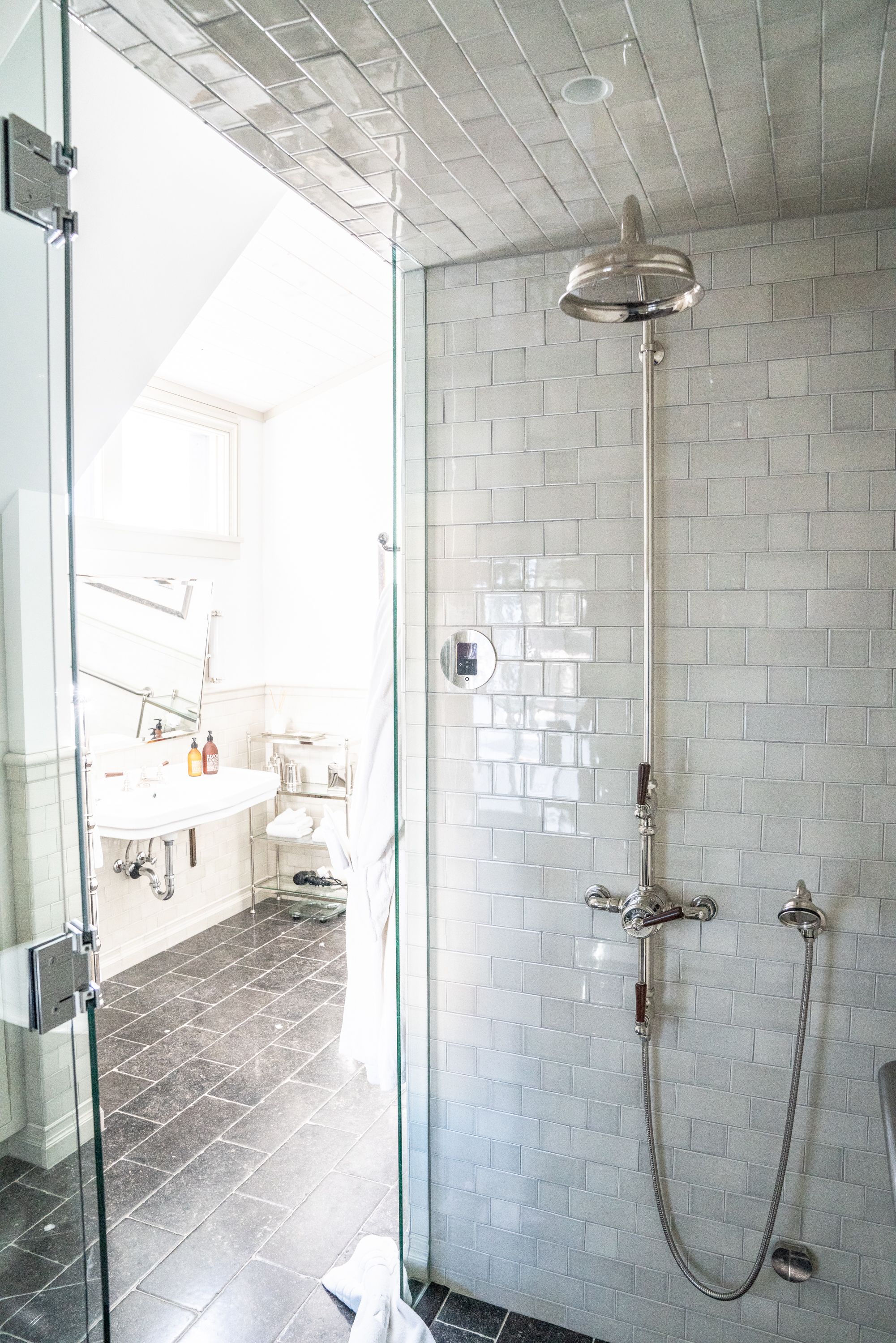 A modern bathroom with a glass shower enclosure, a white tiled wall, and a visible sink area with toiletries.