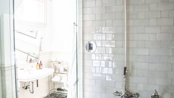 A modern bathroom with a glass shower enclosure, a white tiled wall, and a visible sink area with toiletries.