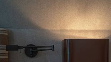 Una mesita de noche ordenada con una lámpara, un control remoto, un libro y un pequeño dispositivo electrónico.