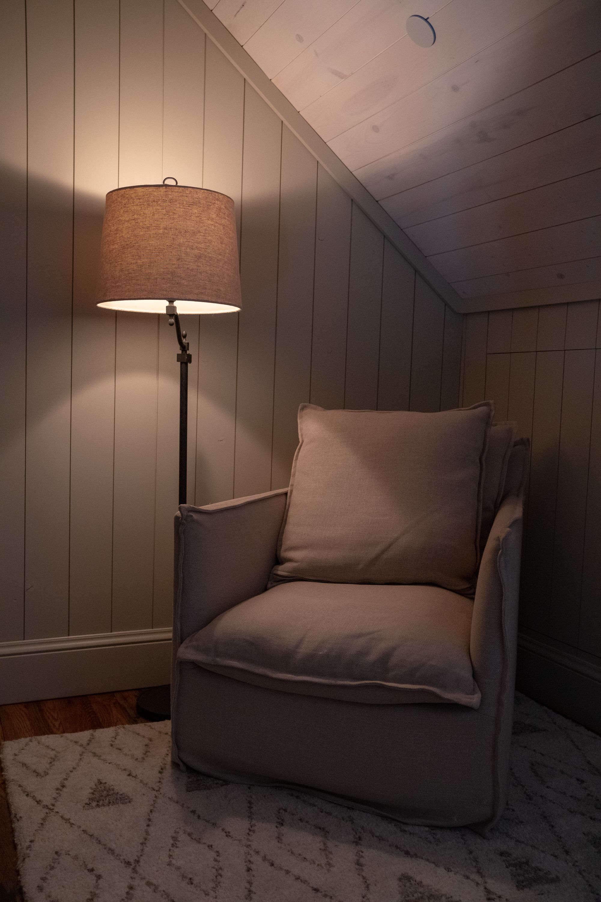 Una habitación de esquina con un sillón color beige, una lámpara de pie y un tapete estampado.