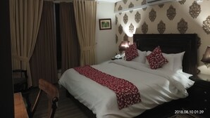 Una habitación de hotel con cama, cortinas, aire acondicionado, lámpara y mesita de noche.