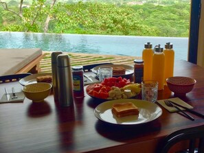 A breakfast table with a view of a lush garden and a pool.