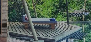 A wooden deck with a bench, surrounded by lush greenery and a hanging chair.