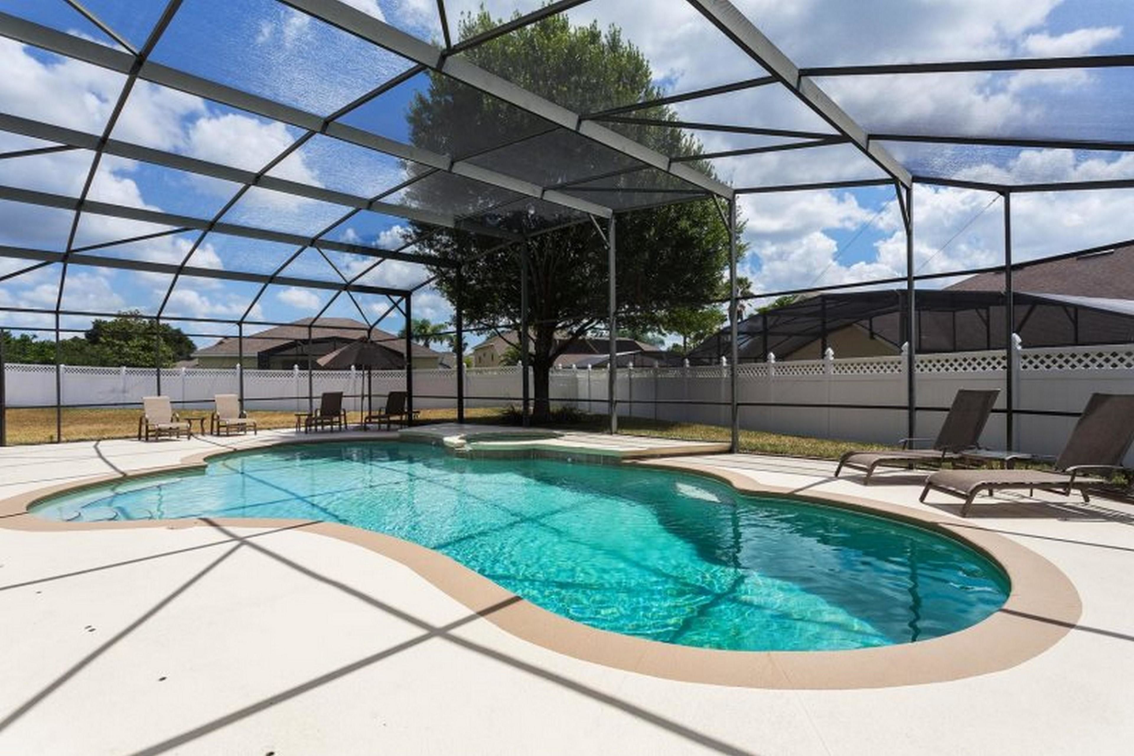 A swimming pool with a covered area, surrounded by lounge chairs and a fence.